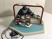 Dominik Hasek goalie figure in black uniform posed in front of red goal on ice rink base, with puck and water bottle.