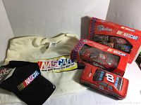 Four item lot: two NASCAR collectible diecast cars in boxes, NASCAR t-shirt, and NASCAR hat.