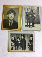 Photo showing three vintage Beatles cards: a colored George Harrison card, a black and white Paul McCartney and John Lennon card, and a black and white group photo of the Beatles, all with printed signatures.