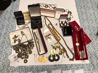 Assorted vintage jewelry laid on blue and white patterned fabric including watches, earrings, necklaces, and silver belt