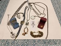 Full lot of assorted jewelry items including necklaces, earrings, fork bangle, bolo tie, and pendant in box; laid out on cloth.
