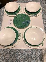 Overhead view of four cereal bowls on matching dinner and lunch plates plus one green Chinoiserie plate at center