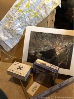 Photo showing cloth map of Toronto hung on wall, large framed aerial photo of Toronto on floor, white drone box, and double-sided puzzle box