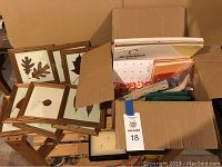 Framed leaf prints stacked showing nine different leaf shapes pressed in wooden frames, resting on top of a cardboard box of art supplies.