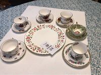 Overview of six tea cups with saucers arranged around a floral Royal Vale cake plate.