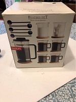 Box showing Bodum Bistro Set with images of coffee maker, cream jar, coffee glasses with cork coasters, and spoons on front side.