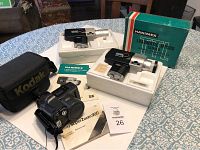 Two Hanimex Loadmatic MP500 Super 8 movie cameras and one Olympus Infinity SuperZoom 300 camera with Kodak branded carrying case and manuals on a table.