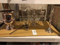 Photo showing the glass pitcher, ice bucket, and two silver candlesticks on a shelf in basement setup.