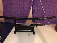 Full view of two decorative swords displayed on a black wooden stand, against a background with purple fabric.