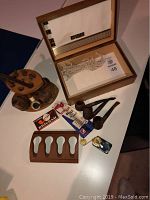 Overview of lot showing 5 wood smoking pipes, pipe stands, a lighter, pipe bit packages, and a wooden box with glass lid.