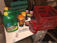 Photo showing all items on white table including Cascade bottles, Armor All wipes, pest control sprays, small pods, clear bottle with red liquid, and red milk crates.