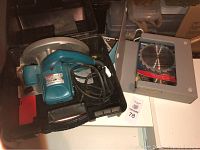 Electric Makita circular saw inside hard black plastic case with visible power cord and blade guard, case open showing tool