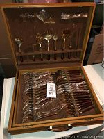 Open wooden box containing the Jean Claude cutlery set arranged in two layers, top with serving utensils and bottom with cutlery pieces like forks, knives, and spoons.