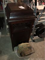 Front view of dark wooden vintage Victrola cabinet phonograph with metal grille, alongside wire basket filled with vintage records