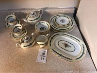 Full view of the 4 place settings including cups, saucers, plates, with teapot, creamer, sugar and serving platter on counter.