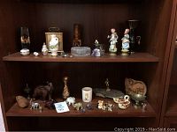 Shelves containing multiple elephant miniatures, porcelain figures, metal bowls, and decorative items including a clock and crystal heart box