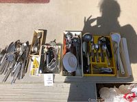 Photo showing multiple boxes and trays with assorted cutlery and utensils including forks, knives, spoons, ladles, peelers, whisks and tongs.