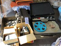 Top view of a box with a small slide viewer, vintage film projectors, film reels, and other vintage electronic equipment.