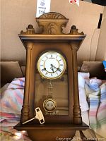 Full front view of the vintage wooden wall clock showing the pendulum and key in front of the glass door.