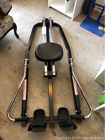 Full view of rowing machine showing metal frame, handles, padded seat, and footrests