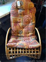 Front view of wicker rocking chair with elephant-patterned cushioned seat and backrest in warm colors.