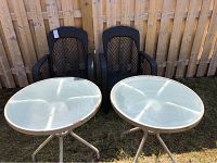 Photo showing two black resin wicker chairs and two round metal tables with glass tops and visible rust on the frames.