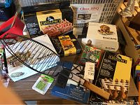 Photo showing assorted boxed BBQ items including GrillPro rib rack and roasting pan, chicken roaster, and other cooking and cleaning tools.