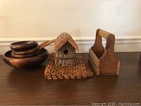 Wood bowls including salad bowls with wooden serving spoon and fork, carved wooden birdhouse on a woven mat, wooden carrier box with cutout sides