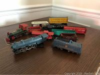 Multiple vintage toy train cars and locomotives in different colors laid out on a table.