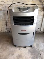 Front view of the Honeywell portable evaporative cooler showing the brand logo, air vents, water level window, and caster wheels.