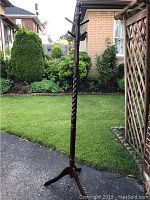 Full view of the wooden coat rack standing outdoors on pavement, showing its height and structure with three curved legs and multiple hooks on top.