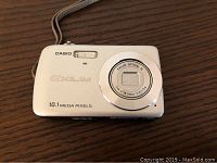 Front view of white Casio Exilim digital camera showing lens, flash, model info, and wrist strap.