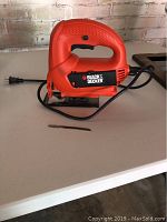 Front and side view of the Black & Decker orange jigsaw with attached power cord, resting on white surface.