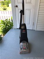Full view of the Bissell carpet cleaner showing upright design, handle, and cord wrapped around the side.