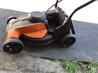 Side view of the orange and black Worx WG775 cordless electric lawn mower showing wheels and battery housing