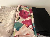 Close-up of folded fabric shower curtains showing muted butterfly and flower pattern on beige background and bright floral design with pink and teal flowers