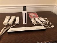 View of all items included: Wii console, three Wii remotes, two Nunchuks, sensor bar, game disc case.