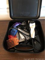 Opened black plastic carrying case showing white Wahl corded clipper, multiple colored clip guides, instruction paper, scissors, and comb.