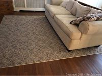 Photo of the Berber area rug showing the corner with the beige sofa on wood floor, displaying the diamond pattern and neutral color.