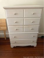 Front view of small white painted wood chest of drawers with six drawers and round knobs.