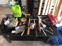 Photo of assortment of hand tools, fasteners, plastic containers, pry bar, safety goggles, and Mold Armor cleaning product on table.