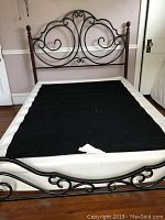 Full size metal scroll bed frame with decorative headboard and footboard, black fabric covering box spring on wooden floor