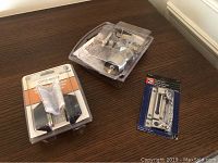 Door hardware items including doorknob, deadbolt, and security chain in original packaging on dark wood surface.