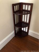 Full view of assembled wood corner shelf with three shelves in dark wood finish, placed in corner.
