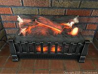 Electric fireplace insert displaying glowing ember and flame effects with artificial logs inside a black metal grate frame, set in a masonry fireplace surround.