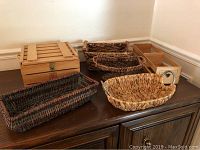 Overall view showing several baskets and wooden boxes on dark wooden furniture, including rectangular wooden box with slatted lid and multiple woven baskets in various shapes and sizes