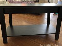 Front view of the black wood composite TV stand showing the top and bottom shelf with legs, positioned on wood floor.