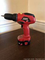 Left side view of red Skil 12V cordless drill placed on a dark surface showing ergonomic grip and power settings.