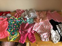 Variety of infant girl clothing including onesies, leggings, and dresses laid out on a dresser showing different colors and patterns