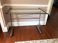 Front angle view of glass top metal desk against wall showing full desk structure and glass top.